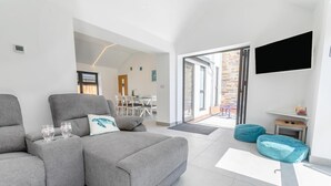 Ein modernes Wohnzimmer mit einem grauen Sofa, zwei Kissen und einem Couchtisch. Im Hintergrund ist eine Essecke mit Tisch und Stühlen zu sehen.