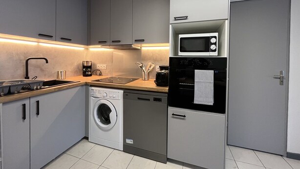 Een moderne keuken met grijze kastjes, een ingebouwde wasmachine, een magnetron en een koffiezetapparaat.