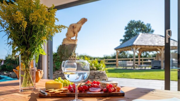 Una mesa con una copa de vino blanco, una tabla de quesos y un jarrón con flores.