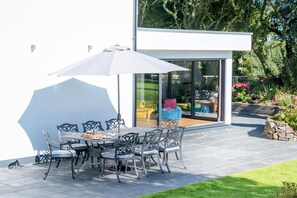 Patio esterno con tavolo e sedie, un ombrellone grande e una porta vetrata che dà su un ambiente interno.