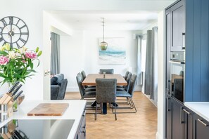 Una cucina moderna con un piano di lavoro in legno, un'area pranzo con tavolo e sedie grigie, e un orologio grande appeso al muro.