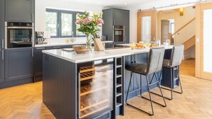 Una cocina moderna con armarios oscuros, una isla central con taburetes de bar, un enfriador de vino empotrado y vistas al exterior a través de amplias ventanas.