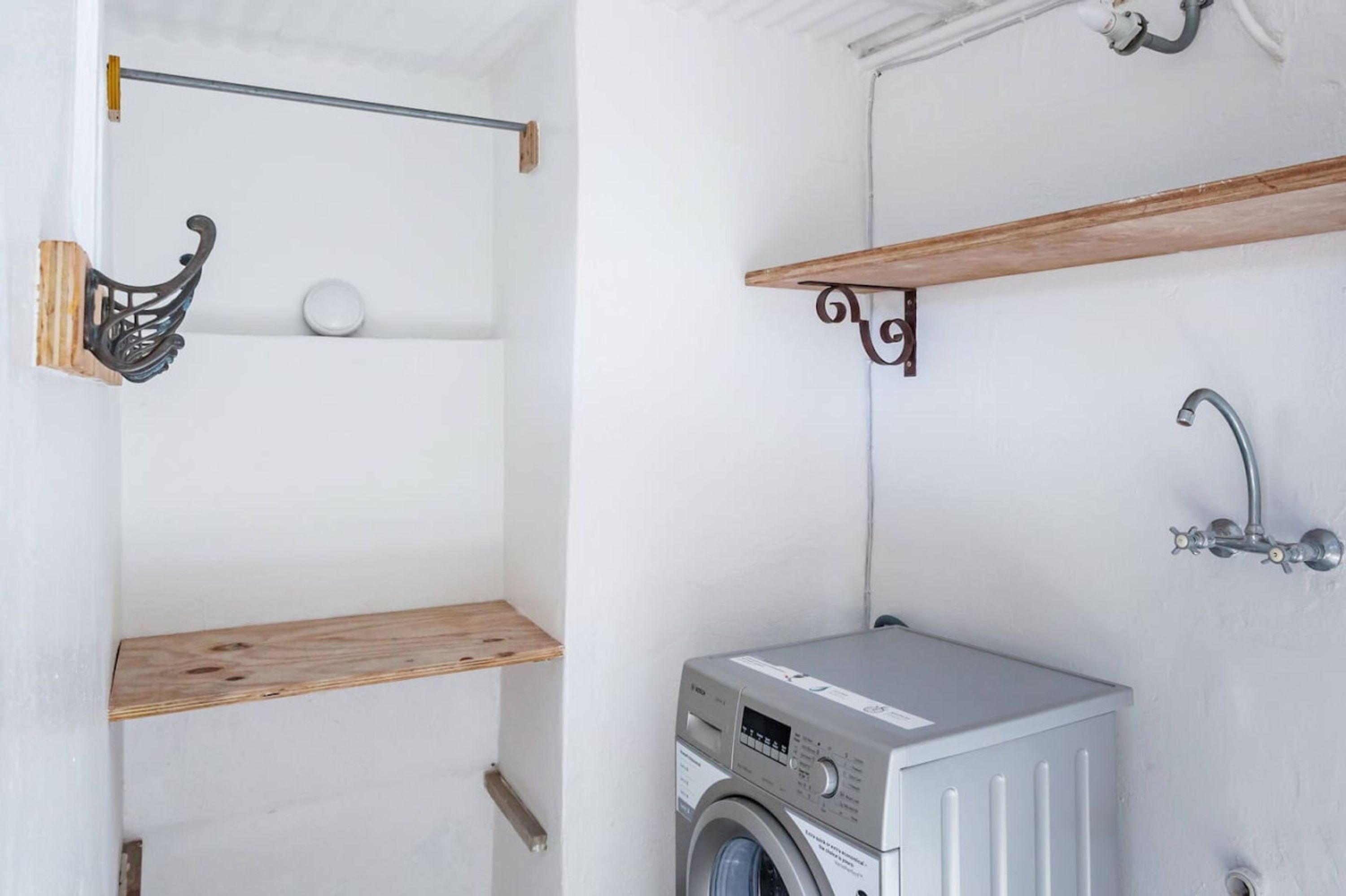 A laundry room with a washing machine, wooden shelves, and a metal rack.
