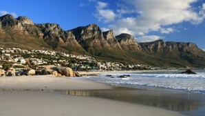 A coastal town with a beach, rocky cliffs, and a mountain range in the background. - 8th Floor- Table Mountain Views|Central & Secure (Cape Town)