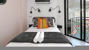 A modern hotel room with a bed, a TV, and a view of a cityscape. - The Flamingo | One Bed | Sea Point Promenade (Cape Town)