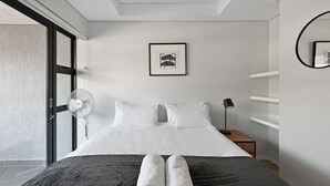 Et moderne hotelværelse med en stor seng, hvide sengetøj, en ventilator, en sengetårnslampe og et billede i ramme på væggen.