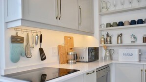 A modern kitchen with white cabinets, a black induction cooktop, a coffee maker, and a bread box labeled "BREAD". - Spacious 3 Bedroom Home | Green Point (Cape Town)