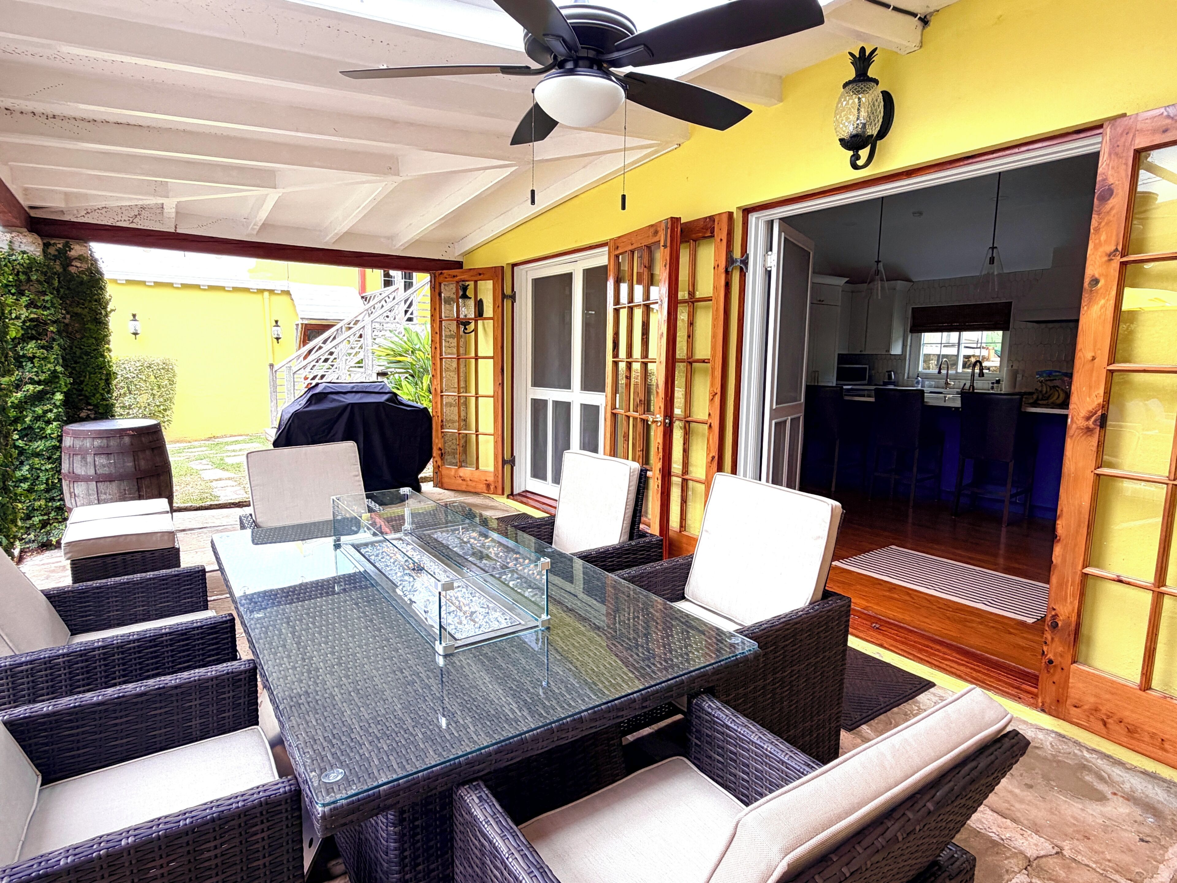 An outdoor dining area with a glass-top table, wicker chairs, and a ceiling fan.