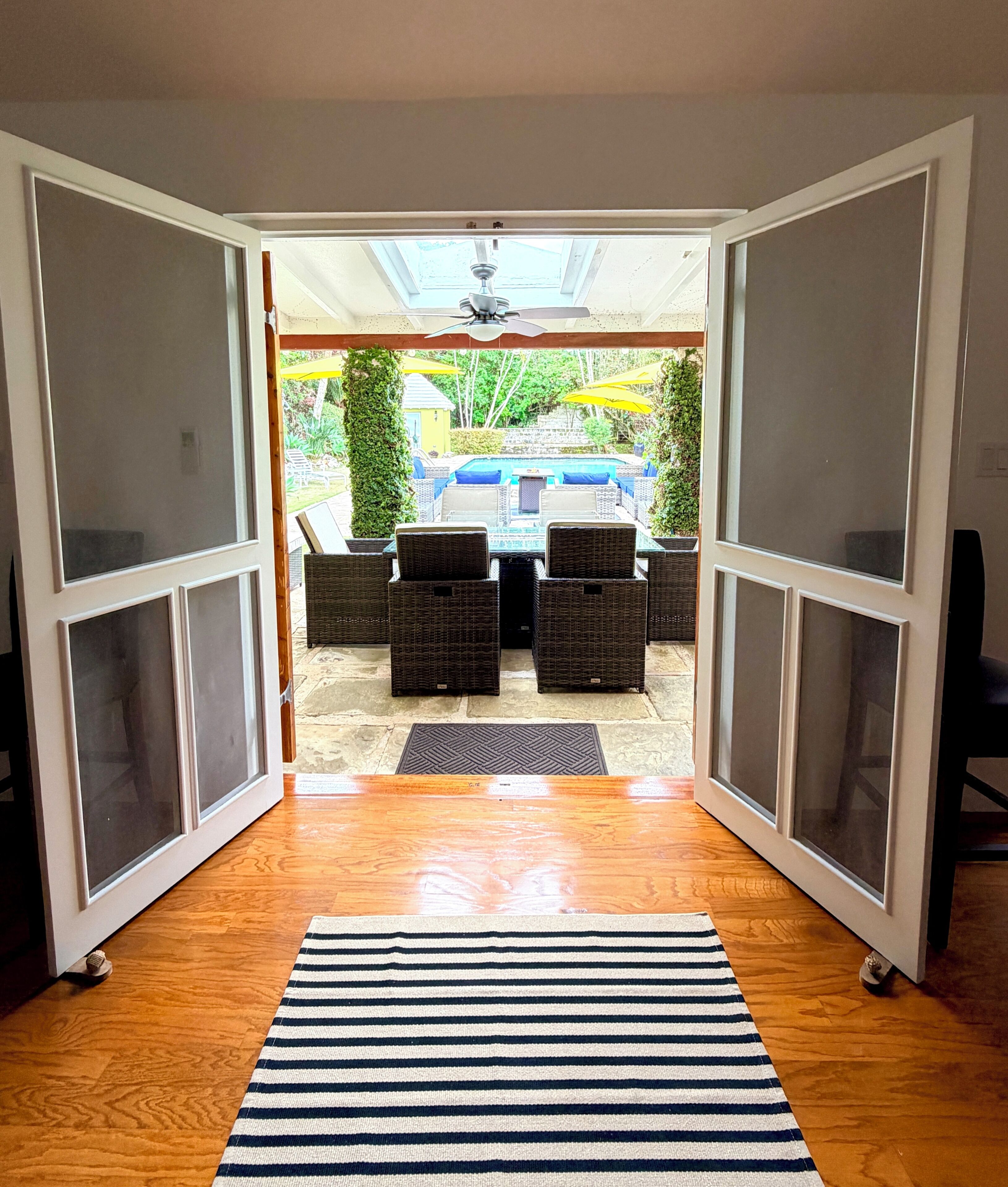 A room with a wooden floor, a striped rug, and a view of an outdoor patio with wicker furniture and umbrellas.