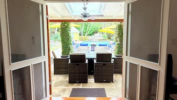 A room with a wooden floor, a striped rug, and a view of an outdoor patio with wicker furniture and umbrellas.