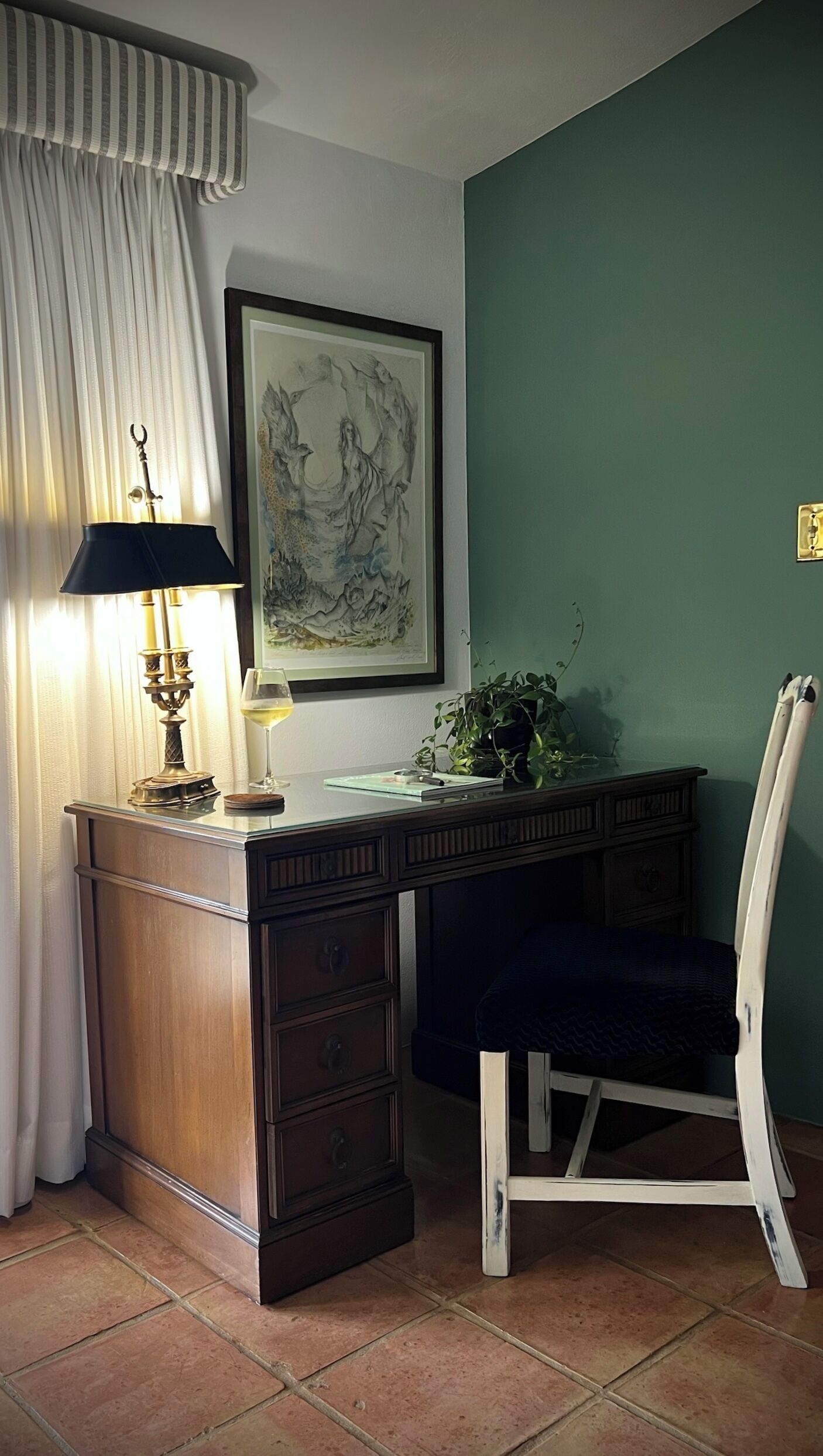 A room with a desk, a chair, a lamp, a framed artwork, and a potted plant.