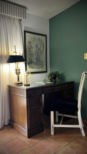 A room with a desk, a chair, a lamp, a framed artwork, and a potted plant.