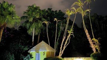 A nighttime view of a swimming pool area with a small gazebo and palm trees.