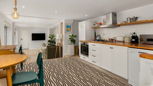 Una cocina moderna con armarios blancos, encimera de madera y horno integrado. Cuenta con un comedor con mesa y sillas de madera, y una alfombra estampada en el suelo.