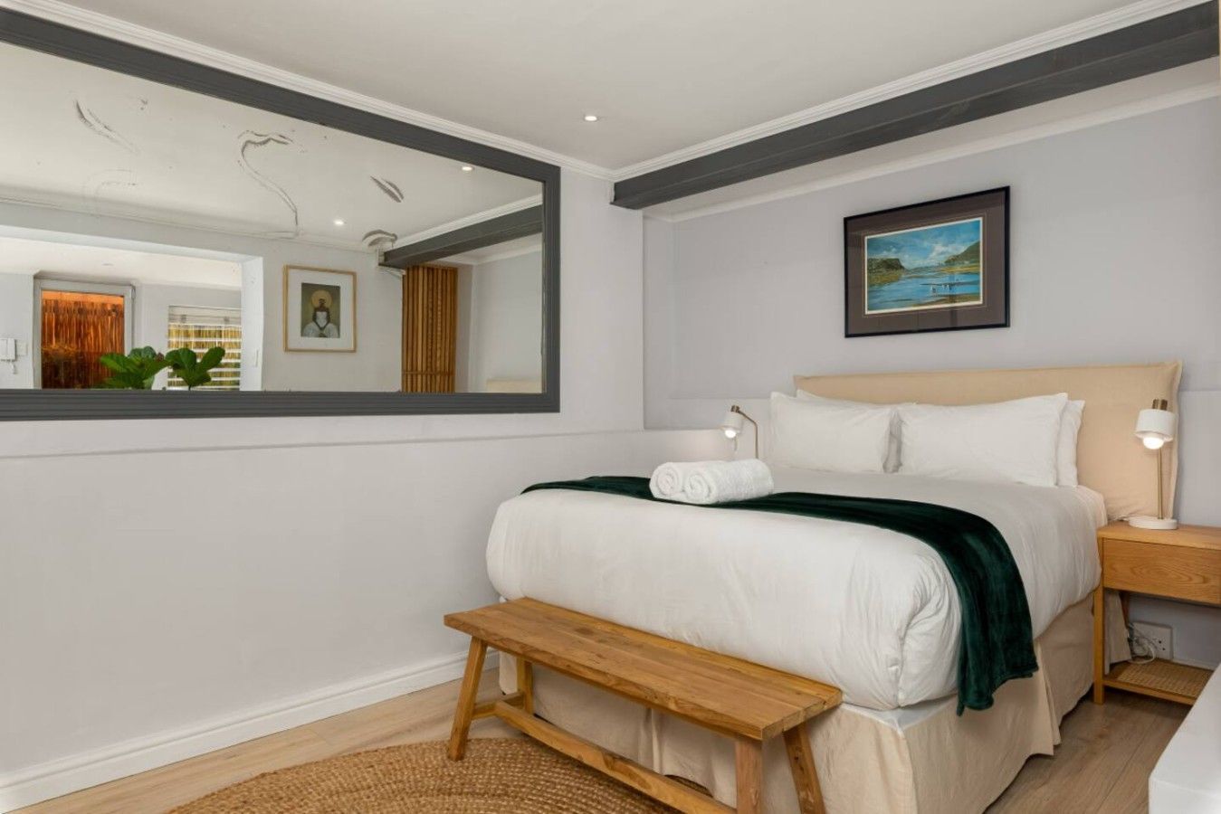 A hotel room with a bed, bedside table, lamp, and a large mirror.
