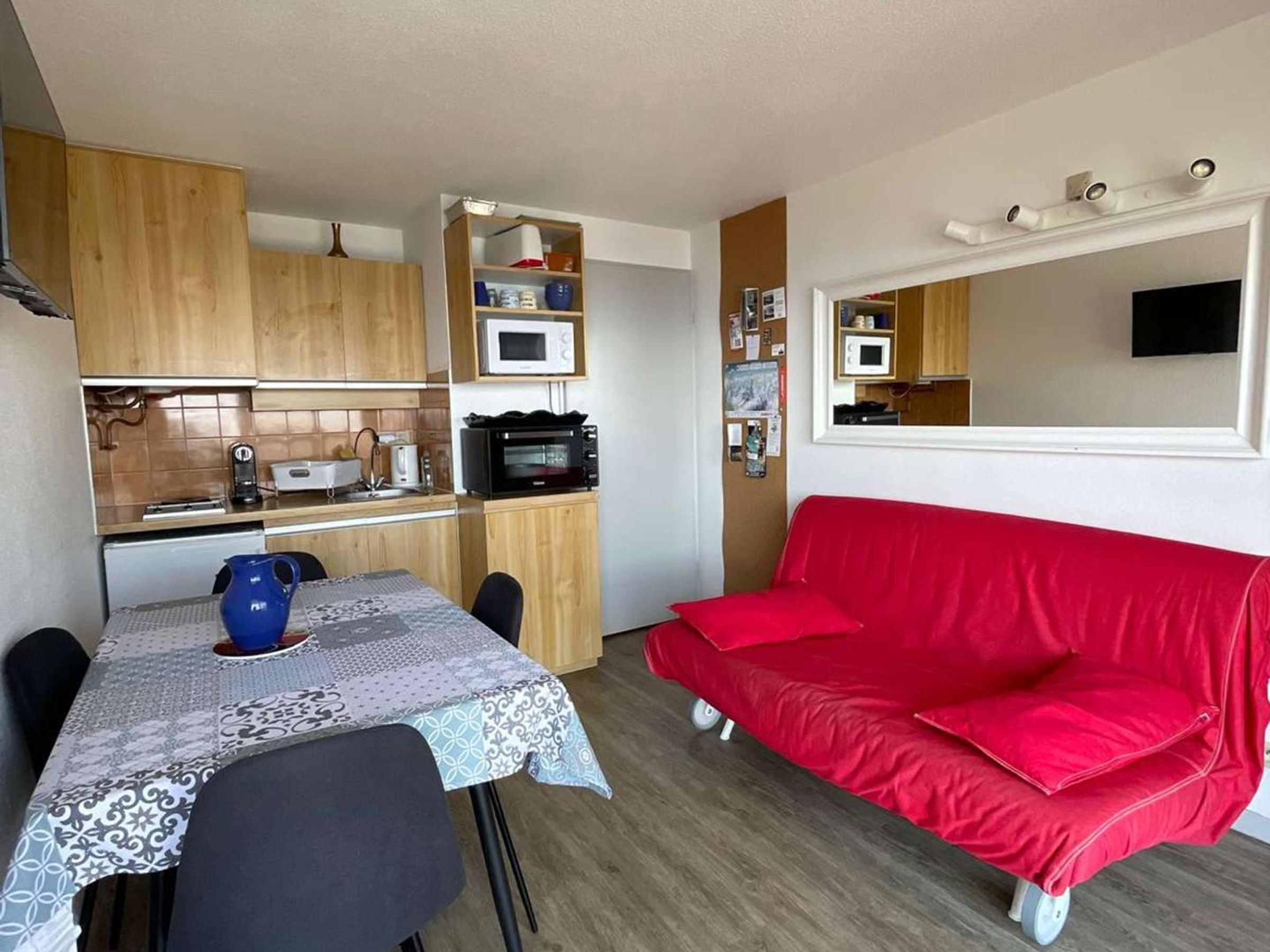 Un espacio habitable compacto con kitchenette, una mesa de comedor con sillas y un sofá rojo.
