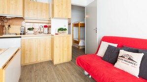 Un ambiente compatto con angolo cottura, un divano rosso e un letto a castello.