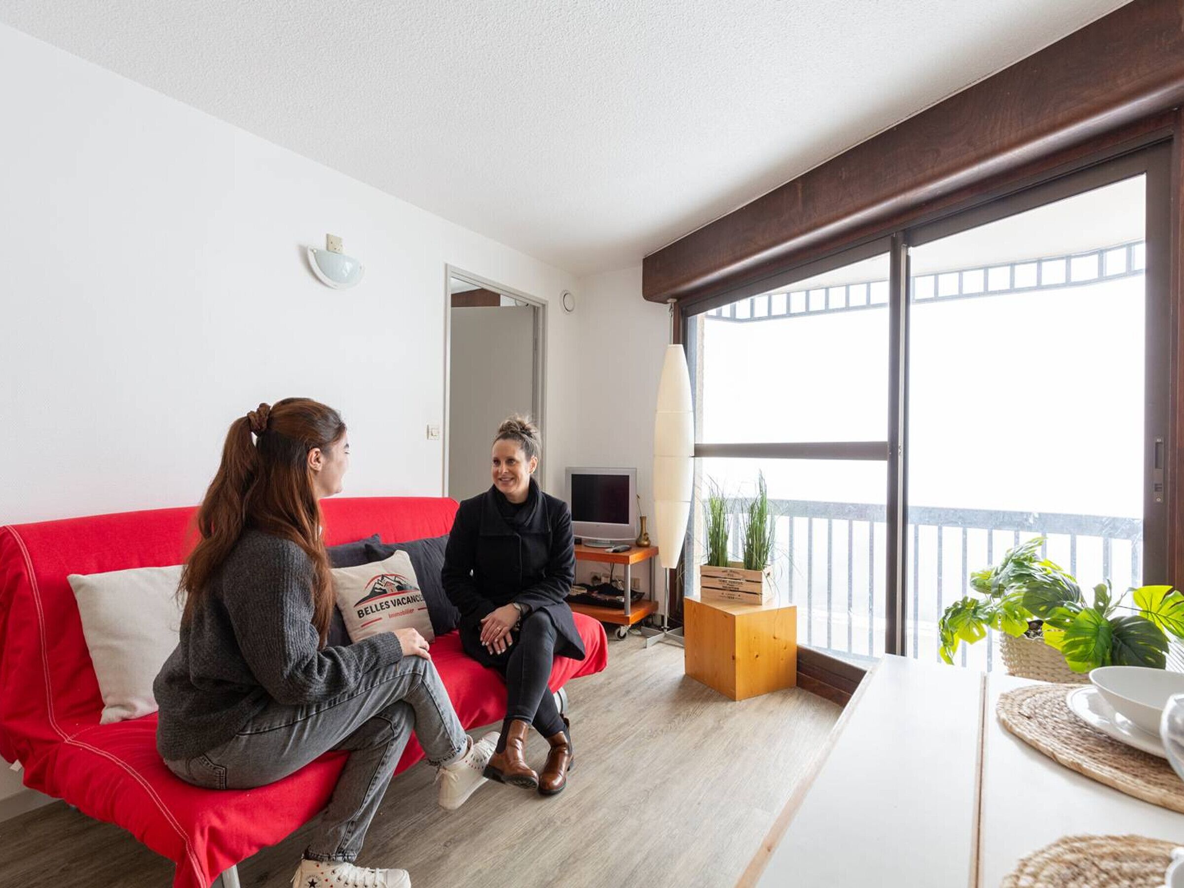A modern living room with a red sofa, a wooden coffee table, and a large window with a balcony view.