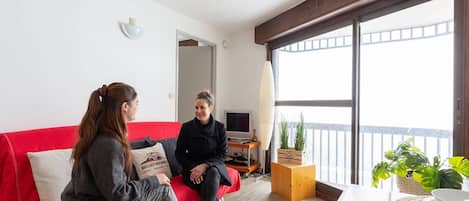 Un salón moderno con un sofá rojo, una mesa de centro de madera y un ventanal con vistas al balcón.