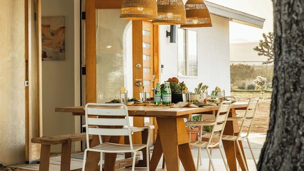 Un espace de restauration en plein air avec une table et des chaises en bois, entouré d’une pergola ornée de lampes en osier suspendues.