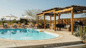 Un jardin avec une piscine, du mobilier d’extérieur, une pergola en bois et un espace barbecue.
