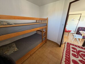 Ein Stockbett mit grauer Bettwäsche, einer Holzleiter und einem kleinen Kopfkissen.