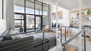 A modern living room with a large window, grey sofa, and a staircase leading to an upper level. - Two Bed | Table Mountain Views | Central (Cape Town)