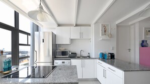 A modern kitchen with white cabinets, a granite countertop, and a large window providing a view of the city. - Two Bed | Table Mountain Views | Central (Cape Town)