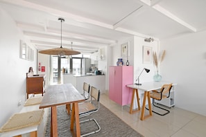 A modern kitchen with white cabinets, a wooden dining table, and a pink cabinet. - Two Bed | Table Mountain Views | Central (Cape Town)
