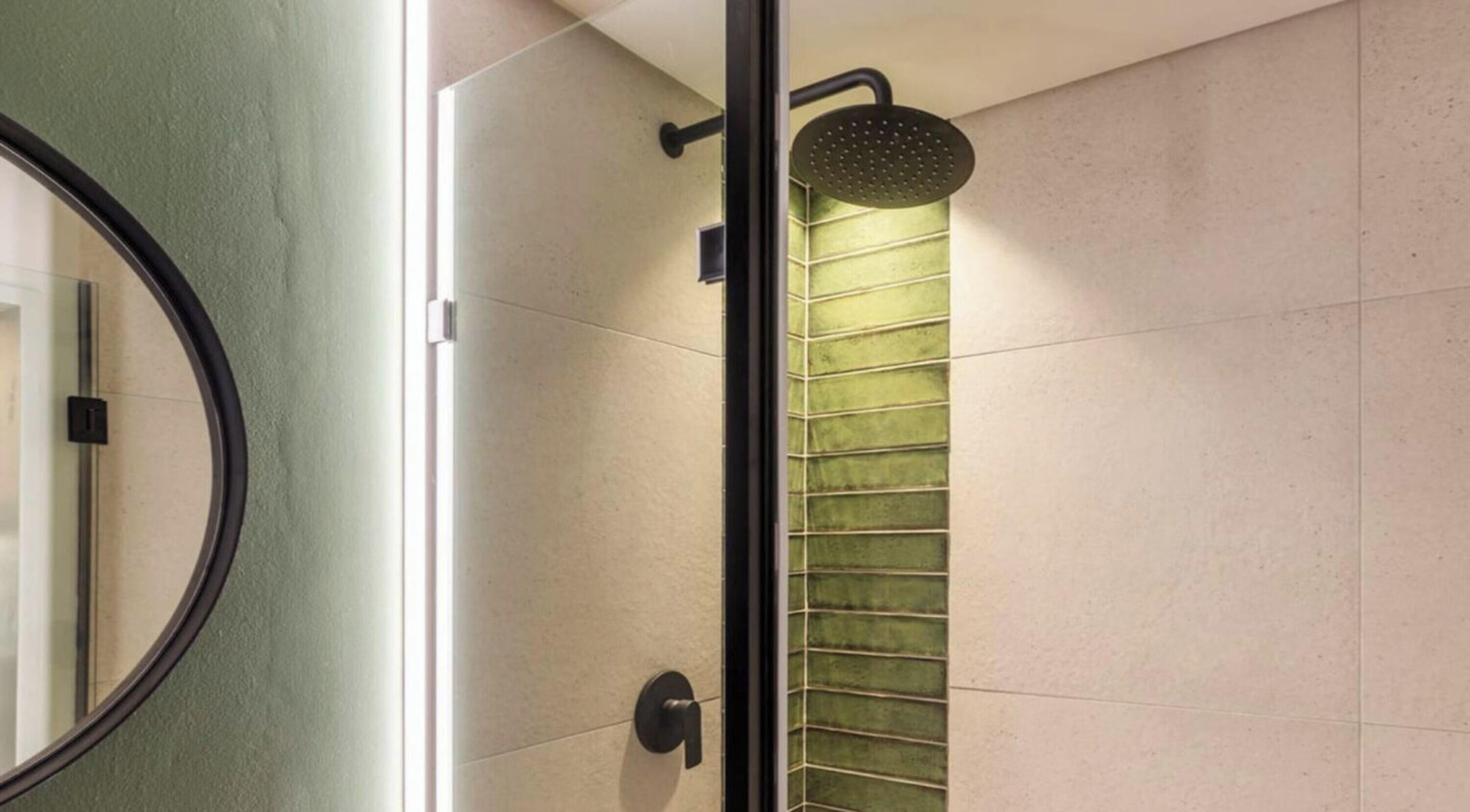 A shower with a green glass door and a black showerhead.