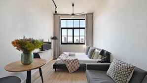 A modern hotel room with a bed, a sofa, a dining table, and a TV. - Modern Apt | Co-Working | East City (Cape Town)