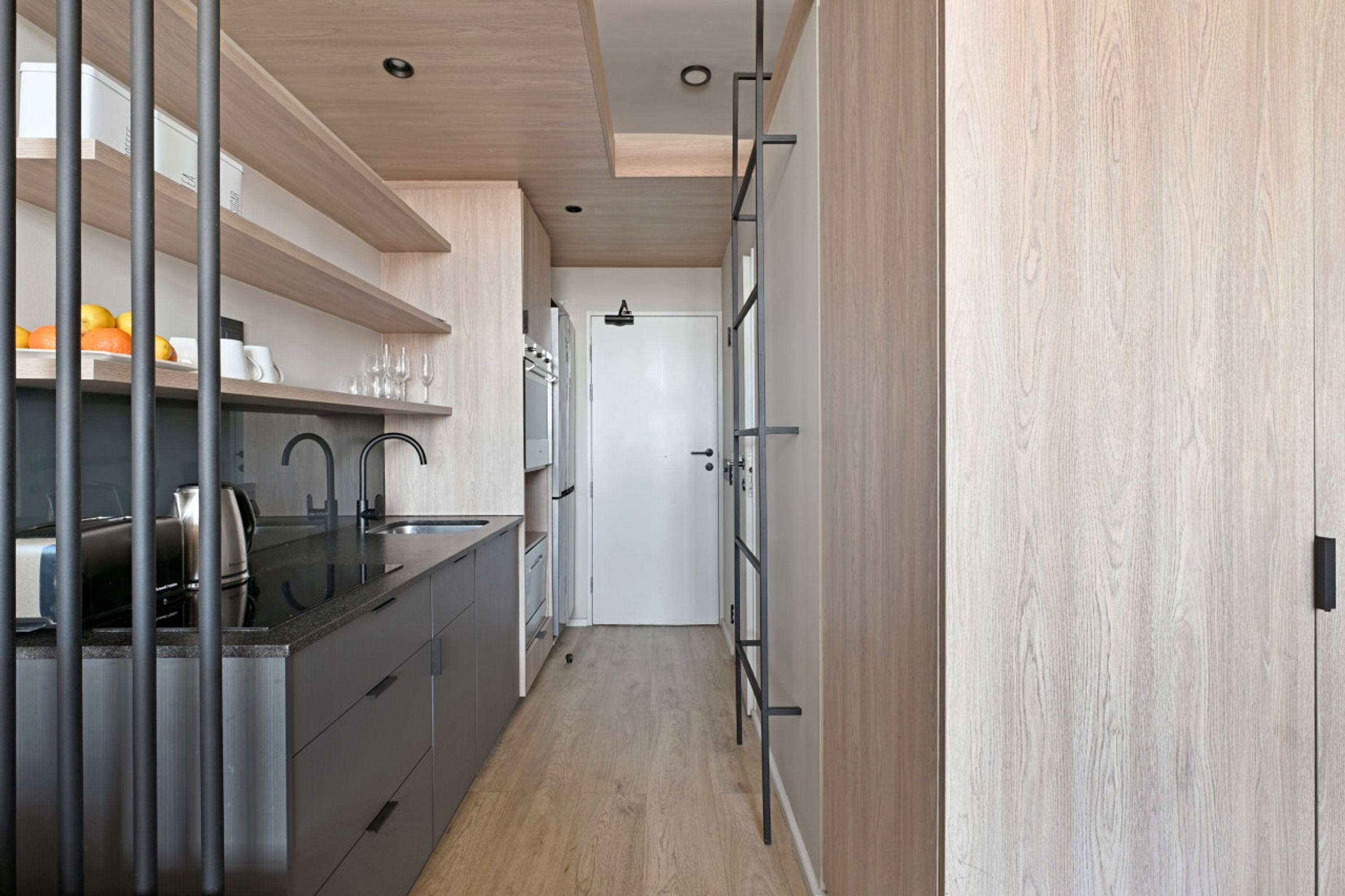 A narrow kitchen with a black countertop, stainless steel appliances, and wooden cabinets.