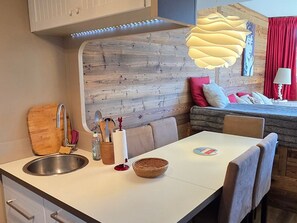 Une cuisine compacte comprenant un évier, une planche à découper en bois et un coin repas avec une table et des chaises.