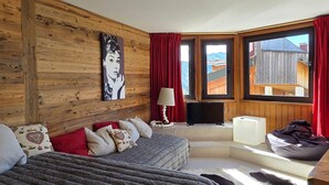 Ett mysigt sovrum med en väggpanel av trä, en säng, en soffa, en tv och utsikt över naturen.