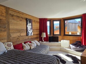 Une chambre confortable avec un mur en bois, un lit, un canapé, une télévision et une vue sur l’extérieur.