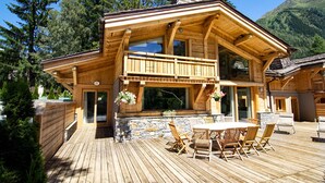 A wooden cabin with a balcony, stone foundation, and a dining area with outdoor furniture. - Chalet Cristal (Chamonix)