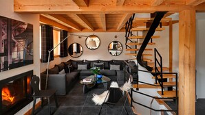 A modern living room with a fireplace, a sofa set, a coffee table, and a staircase. - Chalet Cristal (Chamonix)