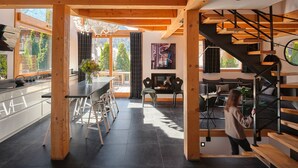 A modern interior with a kitchen, dining area, and living room. There is a staircase with wooden steps and a black railing. - Chalet Cristal (Chamonix)
