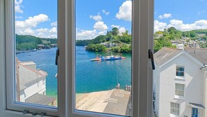 Blick durch ein Fenster auf einen Fluss mit Booten, einen Steg und Gebäude im Hintergrund.