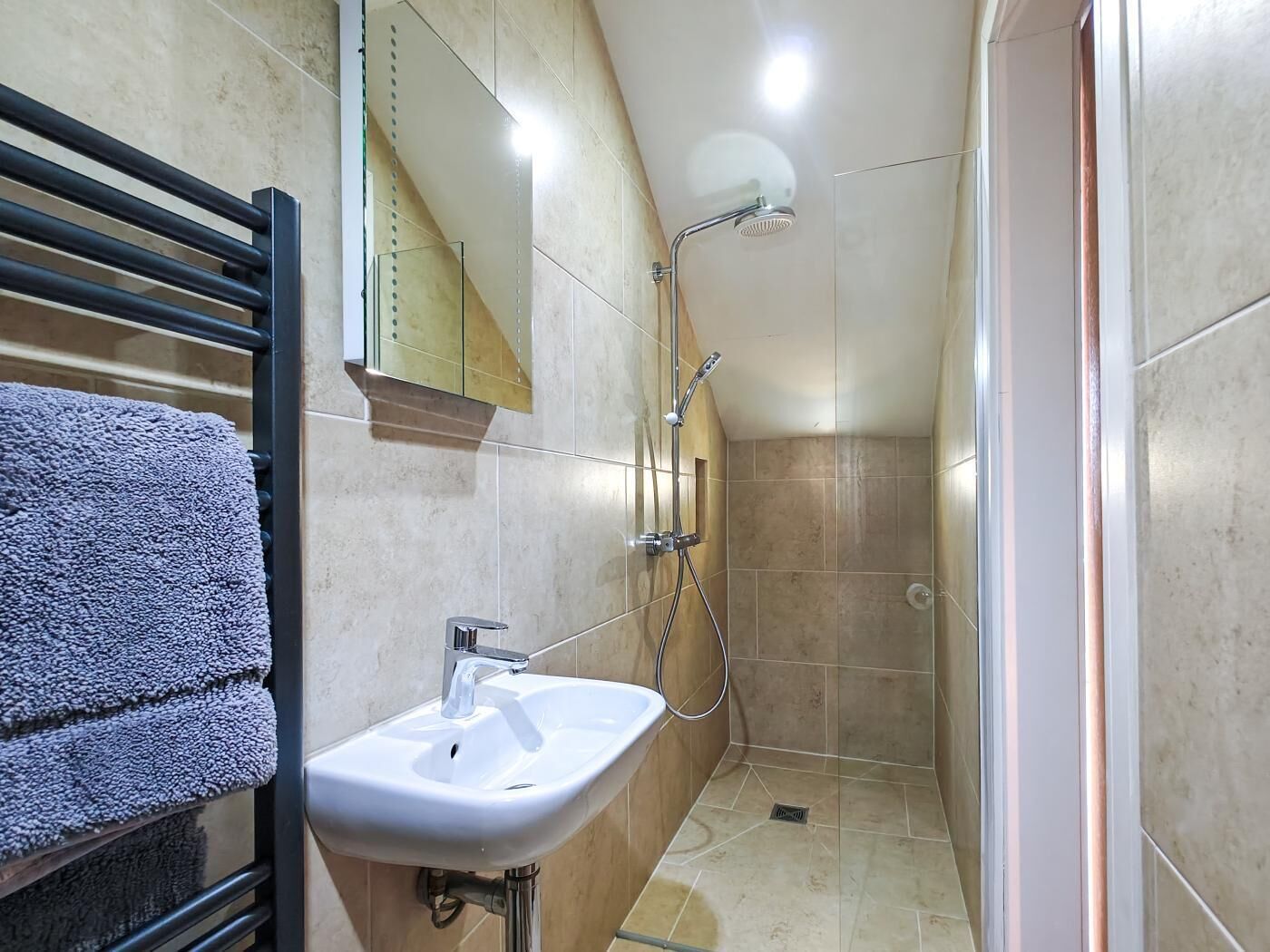 A bathroom with a sink, mirror, towel rack, and shower.