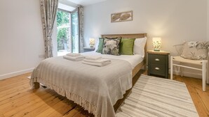 A bedroom with a bed, bedside tables, a nightstand, a window with curtains, and a wall-mounted artwork. - 3 Bed in Torpoint (oc-l32511) (Downderry)