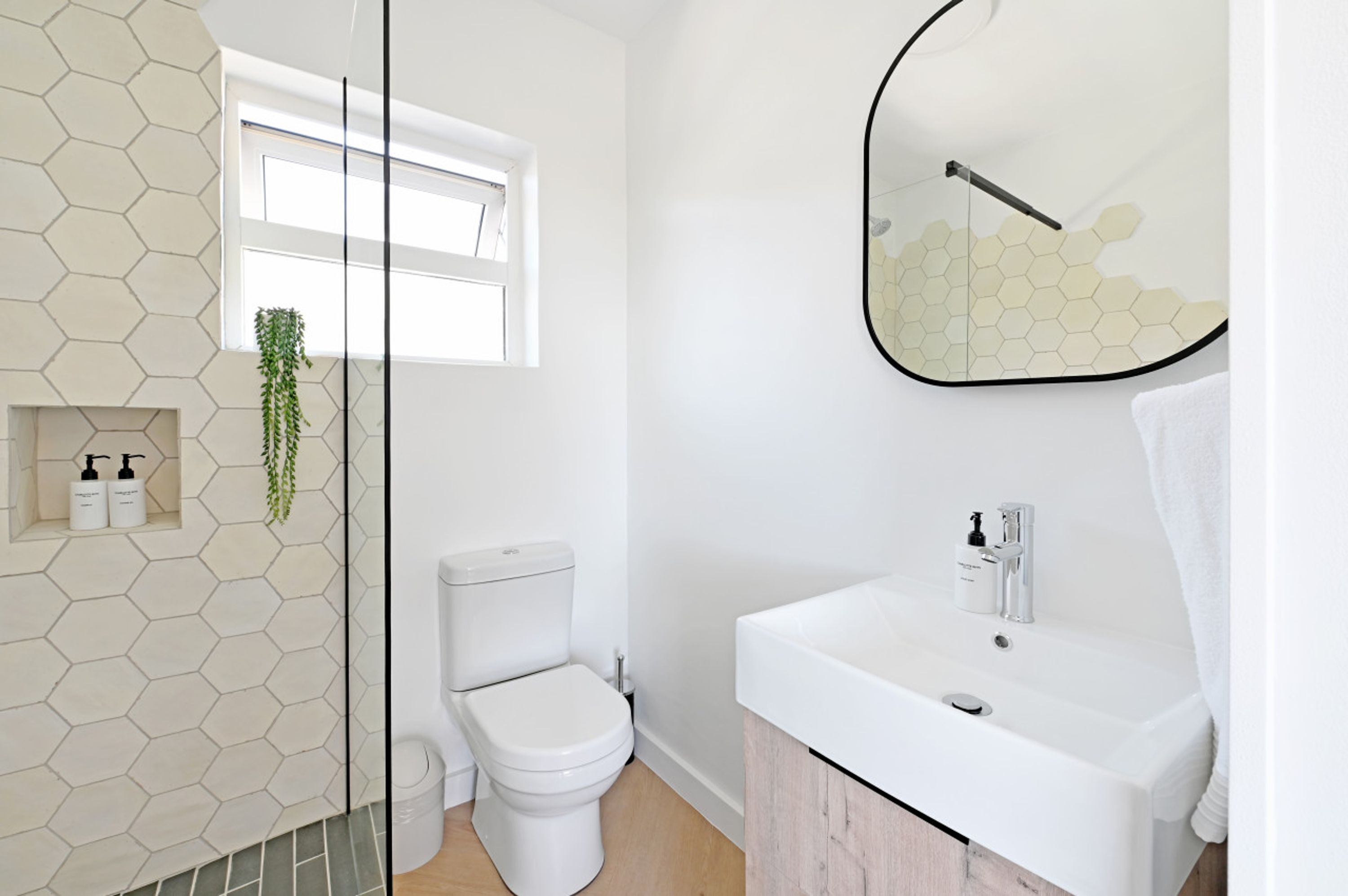 A modern bathroom with a hexagonal tile backsplash, a toilet, a sink with a mirror, and a window.