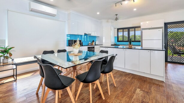 A modern kitchen with white cabinets, a blue backsplash, and a glass dining table with black chairs.