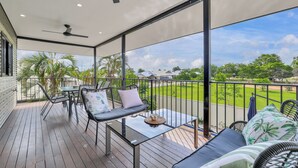 A covered outdoor area with a wooden deck, seating arrangements, and a view of a green landscape.