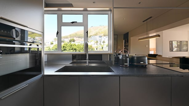 A modern kitchen with a large window, stainless steel appliances, and a minimalist design. - Elegant One Bed | Sea Point | Mountain Views (Cape Town)