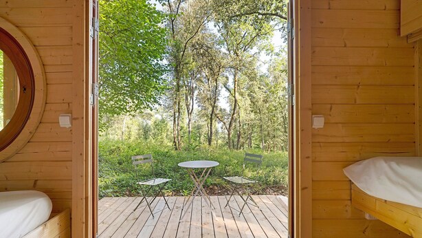 Una cabaña de madera con una cama, una mesita y dos sillas en un área boscosa.