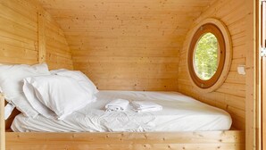 Una habitación de cabaña de madera con cama, almohadas y un ventanal circular.
