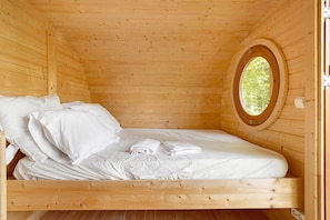 A wooden cabin room with a bed, pillows, and a circular window. - Tiny Home "Unique Accommodation for 3 People" with Shared Pool (Calviac-en-Périgord)