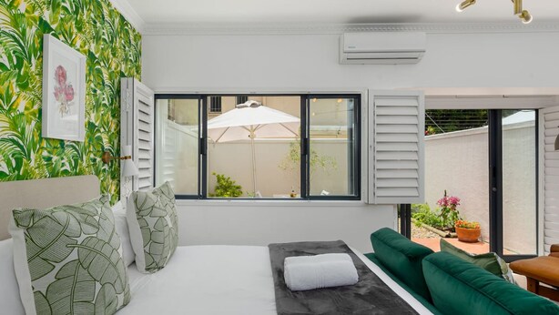 A bedroom with a bed, green sofa, and a window with an umbrella. - Stylish Sea Point Studio in Secure Complex + Patio (Cape Town)