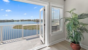 A balcony with a view of a lake and distant buildings, a potted plant, and a window with blinds. - 🏖️🎮🎲Lakefront | Private Pool | A Gamer's Getaway | Destin to Relax (Destin)